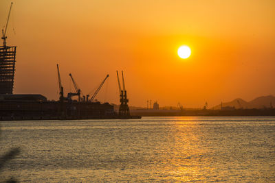 Silhouette cranes at commercial dock against sky during sunset