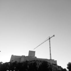 Low angle view of crane by building against clear sky