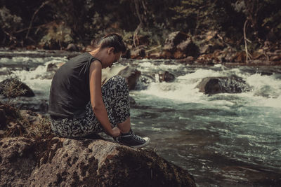 Full length of man sitting on rock in forest