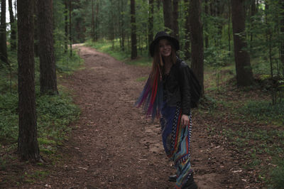 Portrait of smiling young woman standing on footpath in forest