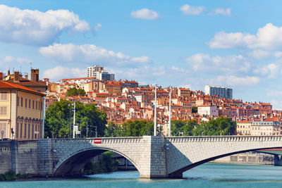 Bridge over river by buildings against sky in city