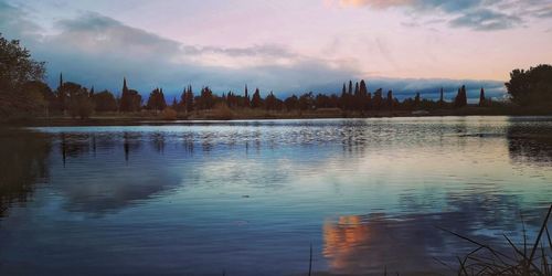 Scenic view of lake by buildings against sky at sunset