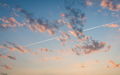 Low angle view of vapor trails and clouds  in sky during sunset