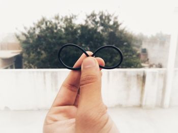 Cropped image of person holding rubber band against sky