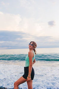 Rear view of woman standing at beach against sky