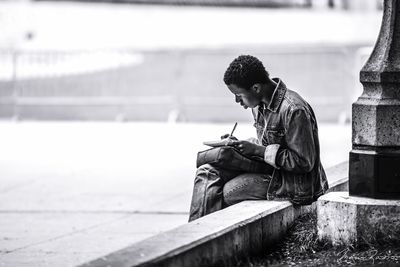 Man writing in book while sitting on retaining wall