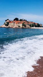 Buildings by sea against clear blue sky