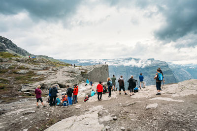 People on cliff mountain against cloudy sky