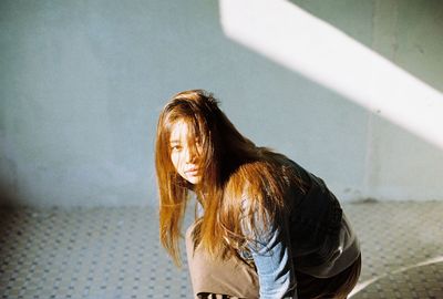 Portrait of young woman crouching on floor against wall