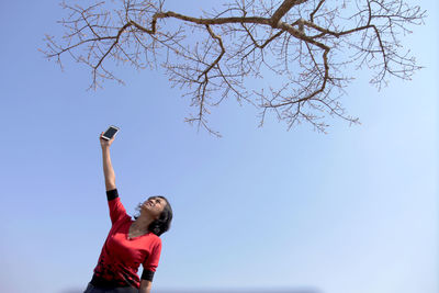 Low angle view of woman with arms raised against clear sky