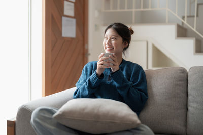 Young woman using mobile phone while sitting on sofa at home