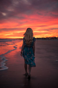 Rear view of young woman at beach against sky during sunset