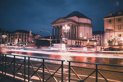 Light trails on street by buildings against sky at night