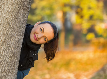 Portrait of smiling woman standing behind tree
