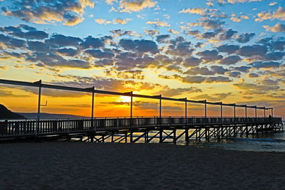 Silhouette bridge over sea against dramatic sky during sunset