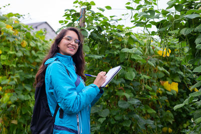 Portrait of young woman standing against plants