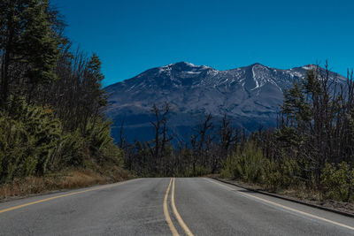 Road amidst trees and mountains against clear blue sky