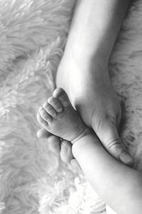 Low section of woman holding baby feet on bed