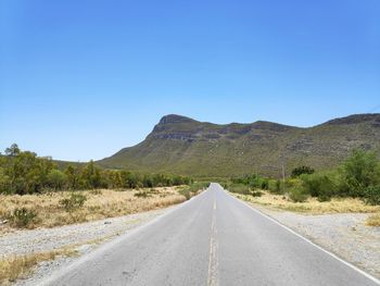 Road leading towards mountains against clear blue sky