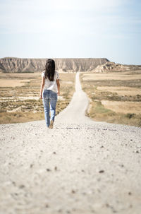 Rear view of woman walking on desert road