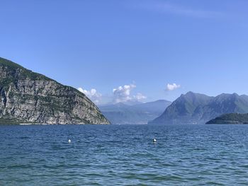 Scenic view of sea by mountains against blue sky