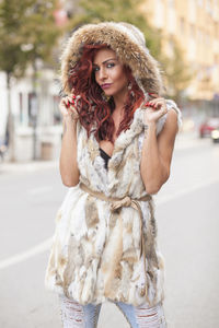 Portrait of young woman in fur coat standing on city street