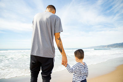 Rear view of father and son at beach against sky