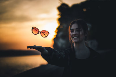 Young woman standing by sea against sky during sunset