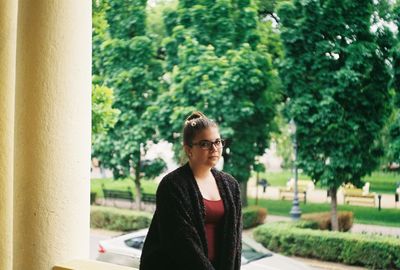 Portrait of young woman standing against trees