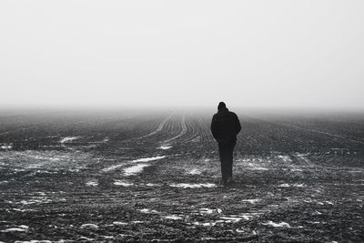 Rear view of man walking on field in foggy weather