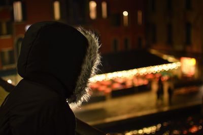 Side view of person on hooded jacket looking at illuminated city