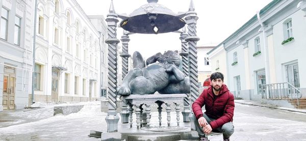 Man sitting on snow covered statue in city