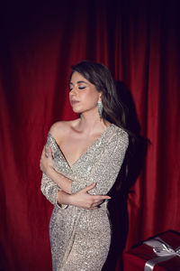 Portrait of young woman standing against red curtain