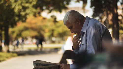 Side view of man reading newspaper while sitting in park