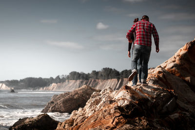 Rear view of man standing on rock against sky