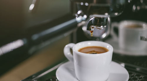 Close-up of machinery dripping coffee in cup on table