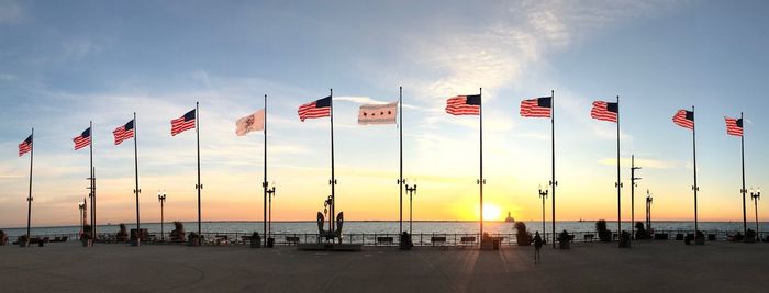 Various flags at beach against sky during sunset