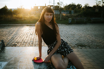 Portrait of young woman sitting outdoors with table tennis racquet 