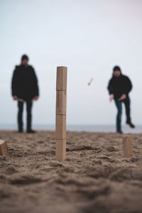 Men aiming for stack of blocks at shore of beach