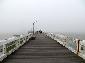 People walking on pier over sea during foggy weather