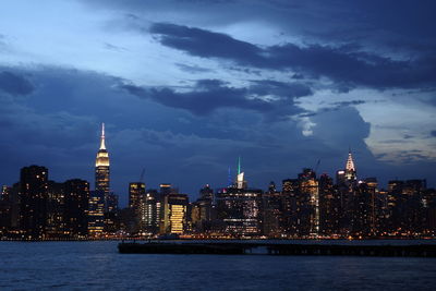 Illuminated buildings in city against cloudy sky