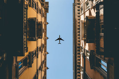 Airplane flying over buildings against clear sky