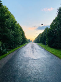 Empty road along trees and plants against sky