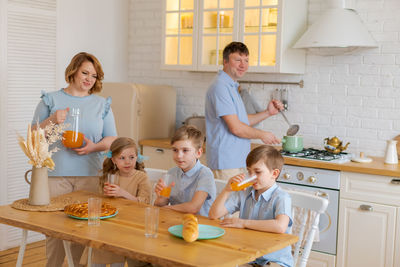Happy caucasian family with children sitting at kitchen table and drinking
