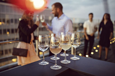 Close-up of wineglasses arranged on table with business professionals in background at terrace during party