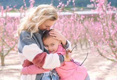 Cute girl embracing mother against cherry trees