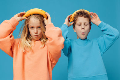 Girl and boy with banana standing against blue background