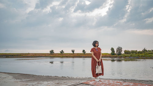 Rear view of woman standing at lakeshore against sky