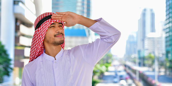 Thoughtful businessman standing in traditional clothing against buildings