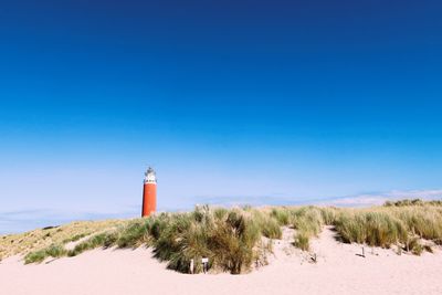 Lighthouse by sea against clear blue sky